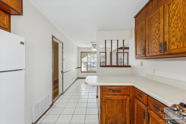 kitchen featuring light tile patterned floors, kitchen peninsula, ceiling fan, and white refrigerator