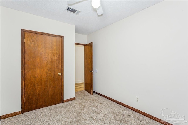 unfurnished bedroom with ceiling fan, light carpet, and a textured ceiling