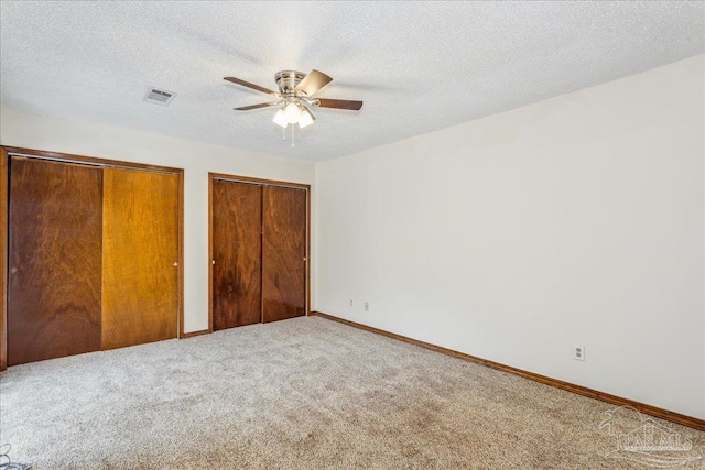 unfurnished bedroom featuring multiple closets, ceiling fan, carpet, and a textured ceiling