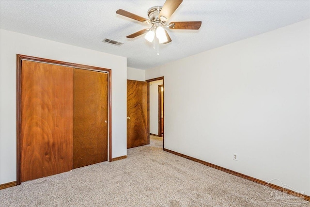 unfurnished bedroom with ceiling fan, a closet, light colored carpet, and a textured ceiling