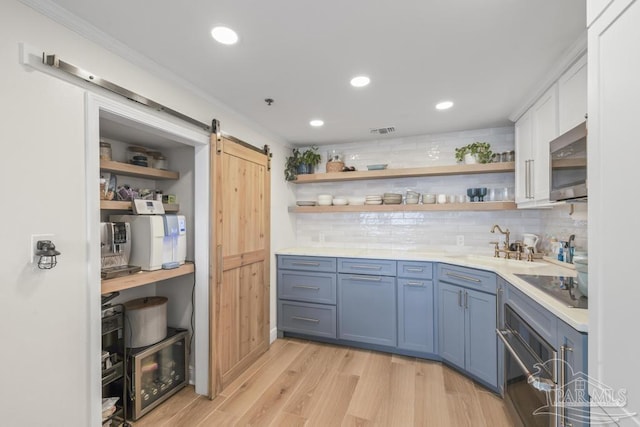 interior space with a barn door, backsplash, oven, light wood-type flooring, and black electric cooktop