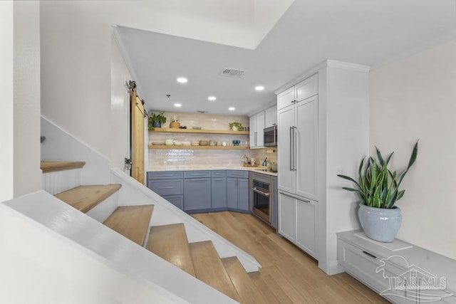 bar with white cabinets, stainless steel appliances, decorative backsplash, light hardwood / wood-style flooring, and a barn door