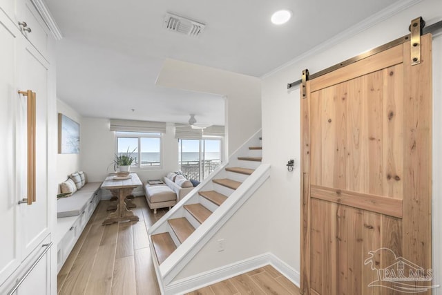 staircase with crown molding, a barn door, and hardwood / wood-style flooring