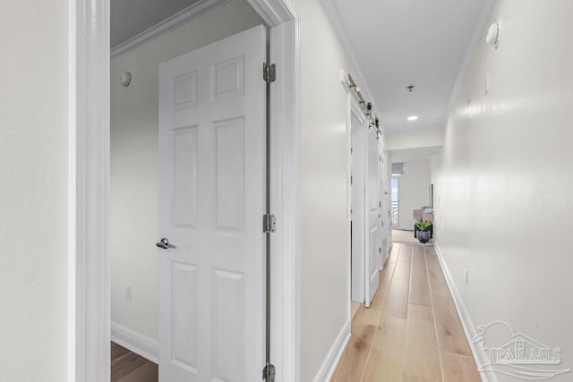 corridor with light wood-type flooring, ornamental molding, and a barn door