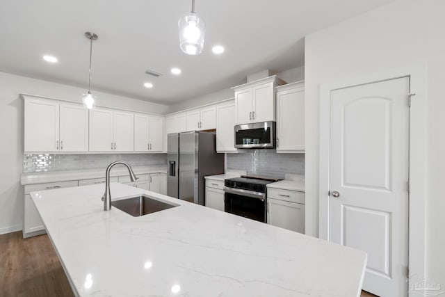 kitchen with white cabinets, decorative light fixtures, a kitchen island with sink, stainless steel appliances, and a sink