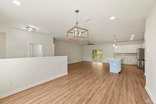 kitchen featuring tasteful backsplash, freestanding refrigerator, open floor plan, white cabinets, and a sink