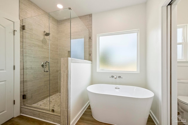 bathroom with toilet, a stall shower, a freestanding bath, and wood finished floors