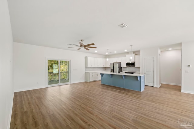 kitchen featuring a breakfast bar, stainless steel appliances, visible vents, light countertops, and open floor plan