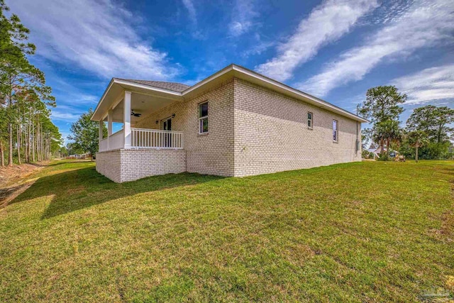 view of side of home with brick siding, ceiling fan, and a yard