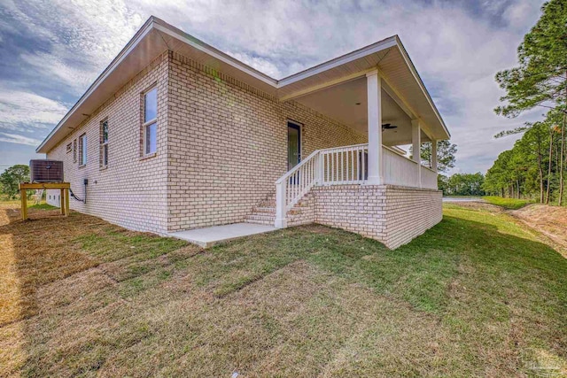 view of side of property with covered porch, central AC, a lawn, and brick siding