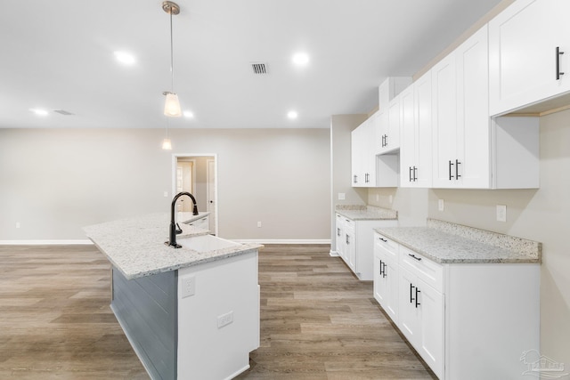 kitchen with hanging light fixtures, white cabinetry, an island with sink, and light stone counters