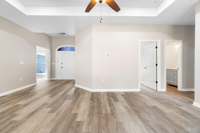 interior space with a tray ceiling, ceiling fan, and light hardwood / wood-style flooring