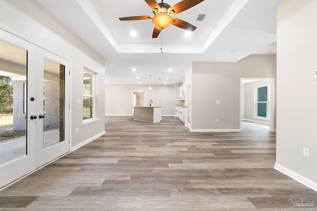 interior space featuring ceiling fan, light hardwood / wood-style flooring, a raised ceiling, and french doors