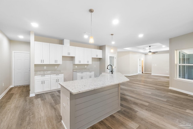 kitchen with white cabinetry, a kitchen island with sink, decorative light fixtures, sink, and light stone counters