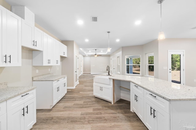 kitchen featuring a center island with sink, hanging light fixtures, light hardwood / wood-style floors, sink, and white cabinetry