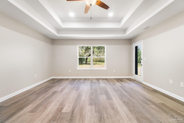 empty room with light hardwood / wood-style flooring, ceiling fan, and a raised ceiling