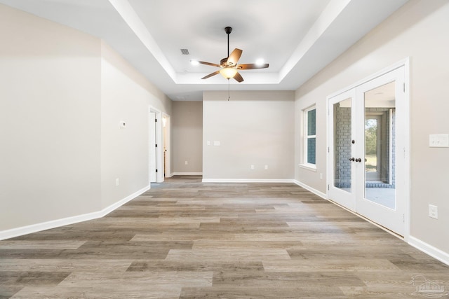 unfurnished room featuring a raised ceiling, french doors, ceiling fan, and light hardwood / wood-style flooring