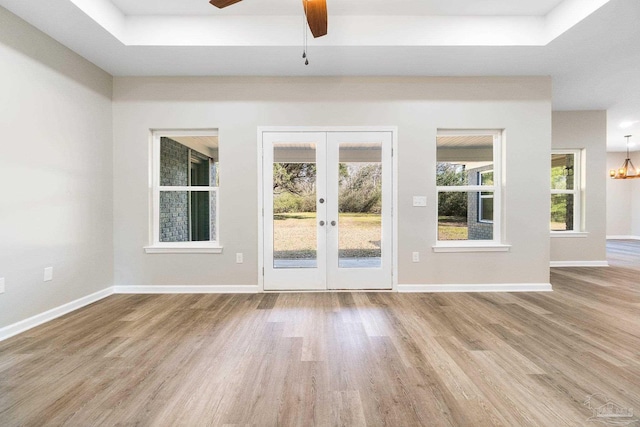 entryway featuring a raised ceiling, light hardwood / wood-style floors, french doors, and ceiling fan with notable chandelier