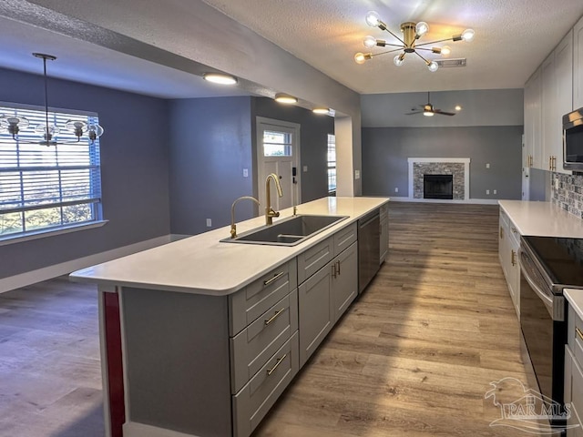 kitchen featuring gray cabinetry, sink, a stone fireplace, a center island with sink, and appliances with stainless steel finishes