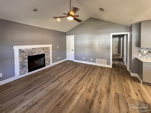 unfurnished living room featuring hardwood / wood-style flooring, ceiling fan, a stone fireplace, and vaulted ceiling