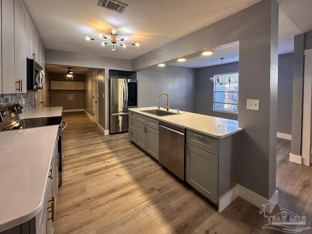 kitchen featuring tasteful backsplash, stainless steel appliances, sink, a notable chandelier, and hanging light fixtures