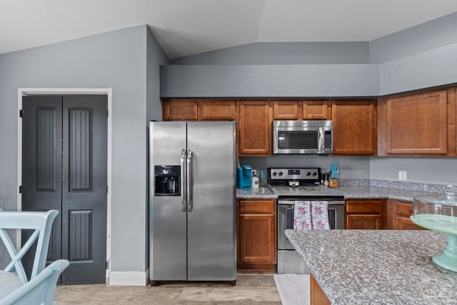 kitchen featuring vaulted ceiling, light wood-style floors, brown cabinets, and stainless steel appliances