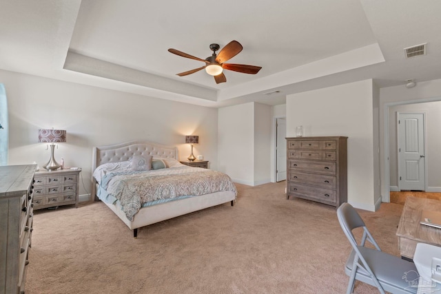 bedroom featuring a raised ceiling, light colored carpet, visible vents, and baseboards