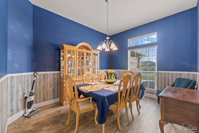 dining area with a wainscoted wall, wood walls, an inviting chandelier, and wood finished floors