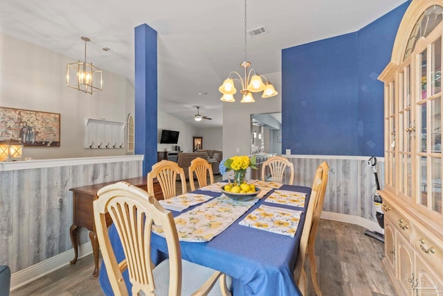 dining room with ceiling fan with notable chandelier, lofted ceiling, wood finished floors, and a wainscoted wall