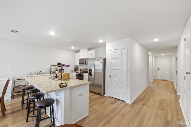 kitchen featuring appliances with stainless steel finishes, white cabinetry, a kitchen island with sink, light hardwood / wood-style floors, and a kitchen bar