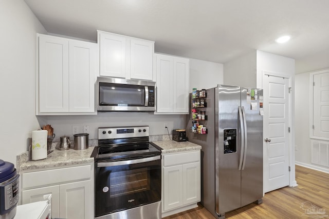 kitchen with appliances with stainless steel finishes, white cabinets, and light hardwood / wood-style flooring