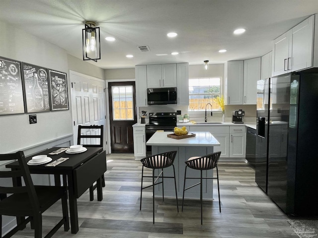 kitchen with black appliances, light hardwood / wood-style flooring, sink, and a kitchen island