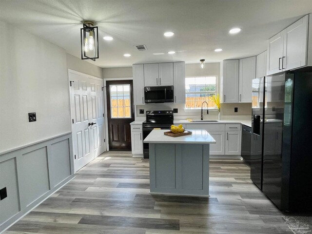 kitchen featuring light hardwood / wood-style flooring, a center island, black appliances, decorative light fixtures, and sink