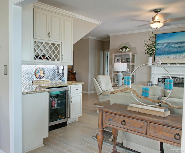 kitchen featuring backsplash, ornamental molding, light stone countertops, ceiling fan, and beverage cooler