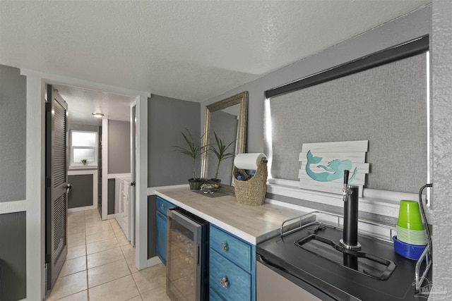 kitchen with a textured ceiling, light tile patterned flooring, blue cabinets, beverage cooler, and light countertops