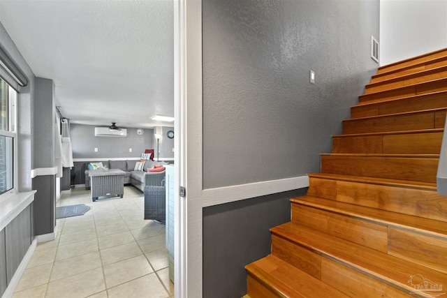 staircase with baseboards, visible vents, a textured wall, a wall unit AC, and tile patterned floors