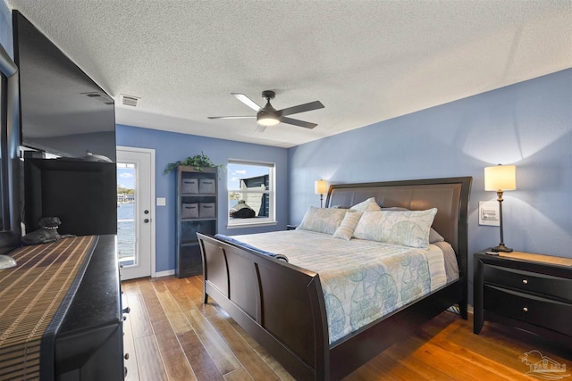 bedroom featuring access to exterior, multiple windows, a ceiling fan, and wood finished floors