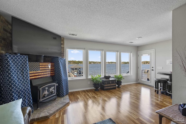 living room featuring baseboards, visible vents, wood finished floors, a wood stove, and a textured ceiling