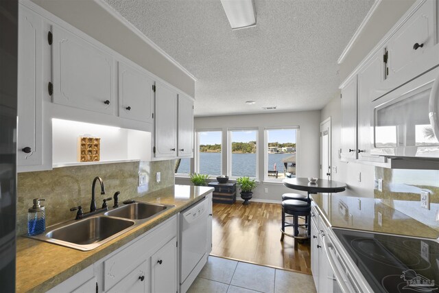 kitchen with light tile patterned floors, decorative backsplash, white cabinetry, a sink, and white appliances