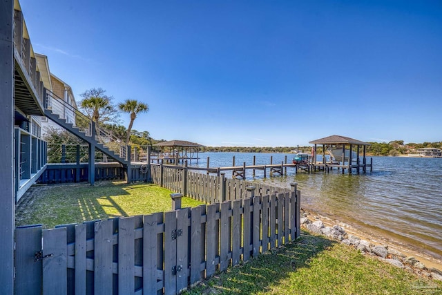 view of dock with a water view, a yard, and a fenced backyard