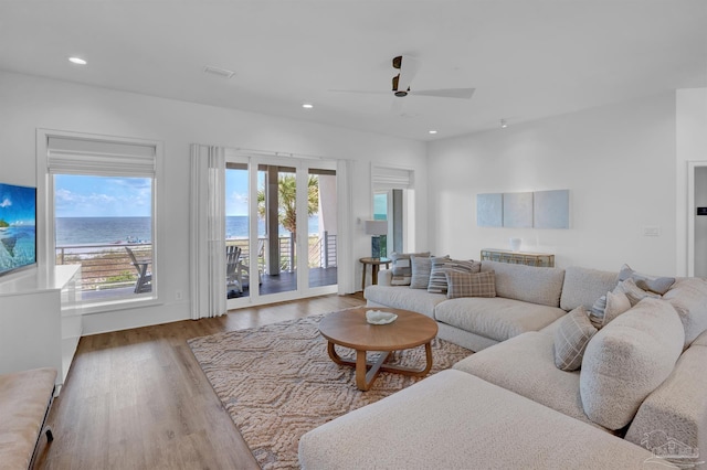 living room with light hardwood / wood-style flooring, a water view, ceiling fan, and plenty of natural light