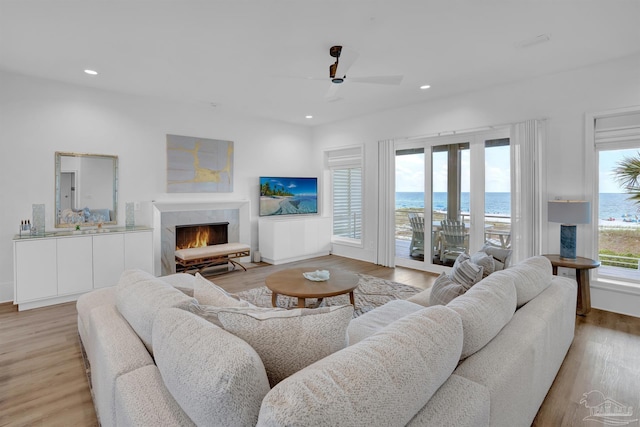 living room with a high end fireplace, ceiling fan, and light hardwood / wood-style floors