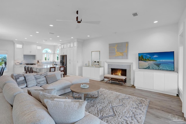 living room with ceiling fan, light wood-type flooring, a high end fireplace, and plenty of natural light