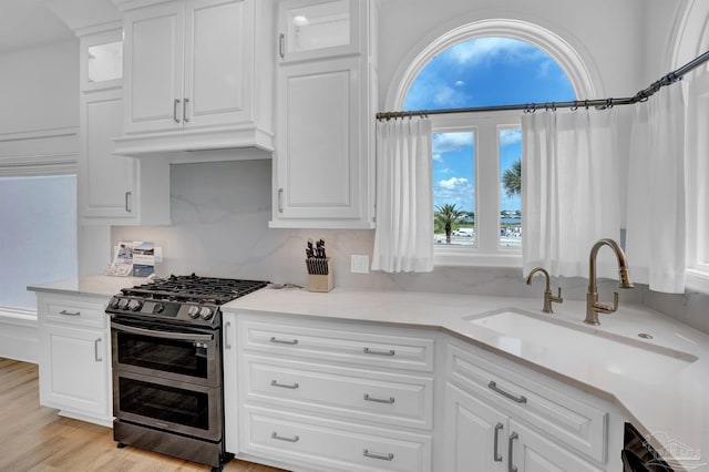 kitchen featuring white cabinetry, light hardwood / wood-style flooring, decorative backsplash, double oven range, and sink