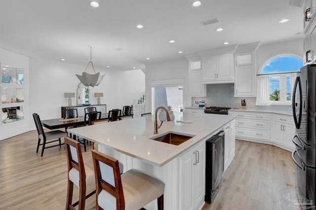 kitchen with sink, light hardwood / wood-style flooring, a center island with sink, and black refrigerator