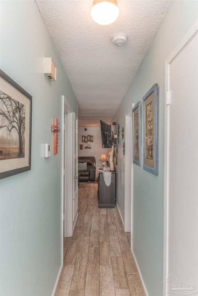 hall featuring wood tiled floor, baseboards, and a textured ceiling