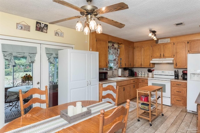 kitchen featuring under cabinet range hood, white appliances, a sink, light countertops, and brown cabinetry