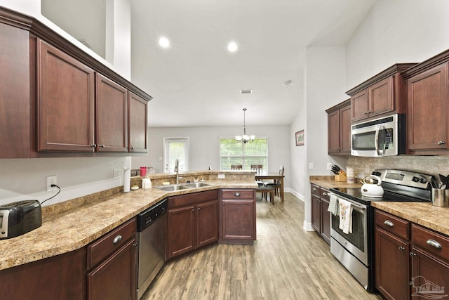 kitchen with stainless steel appliances, a sink, light wood-type flooring, a notable chandelier, and a peninsula