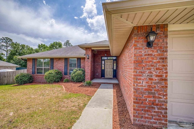 doorway to property featuring fence, a yard, a shingled roof, and brick siding