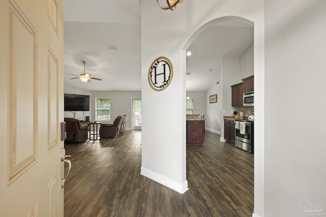 corridor with visible vents, baseboards, arched walkways, dark wood-style flooring, and vaulted ceiling